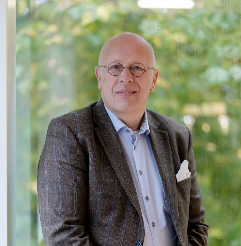 Lachende man met bril en geruit colbert voor een groene, onscherpe achtergrond.