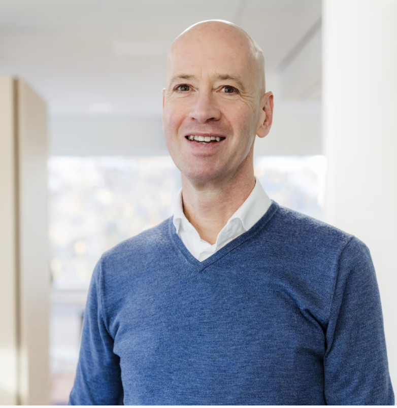 Man met blauwe trui voor een onscherpe kantoorachtergrond.