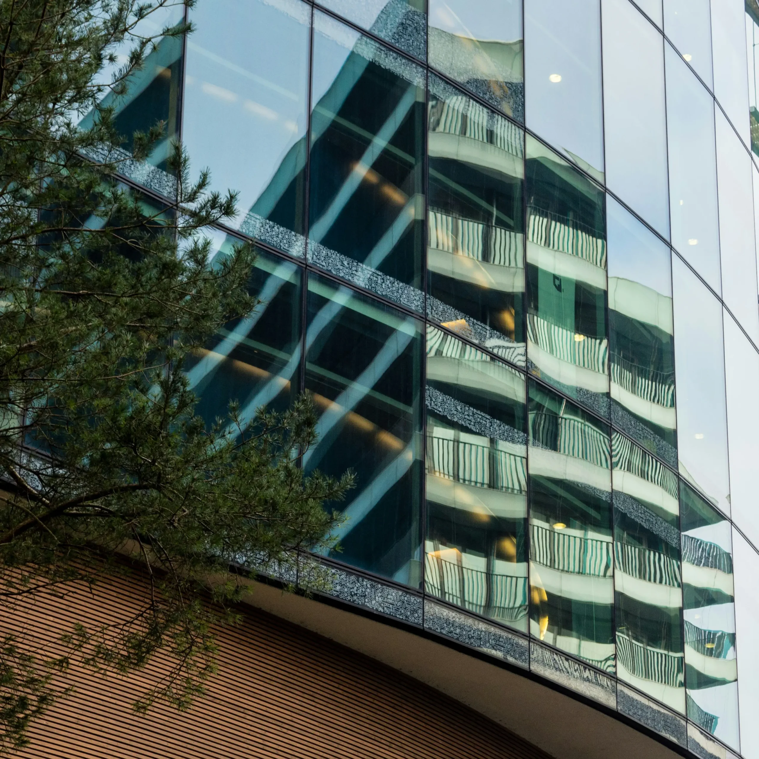 Glazen gevel van een modern gebouw waarin een ander gebouw weerspiegeld wordt.