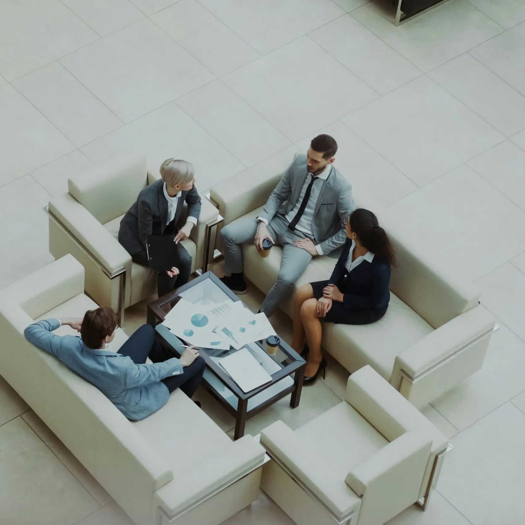 Vier mensen in zakelijke kleding zitten in een zithoek rond een tafel met documenten en laptops.