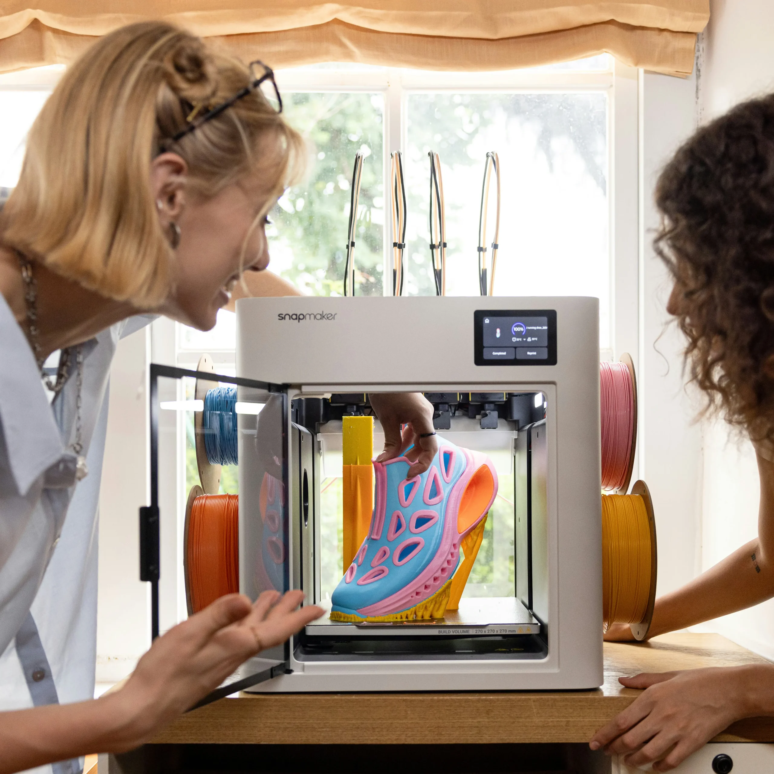 Twee mensen bekijken een kleurrijk 3D-geprint object dat uit een printer wordt gehaald.