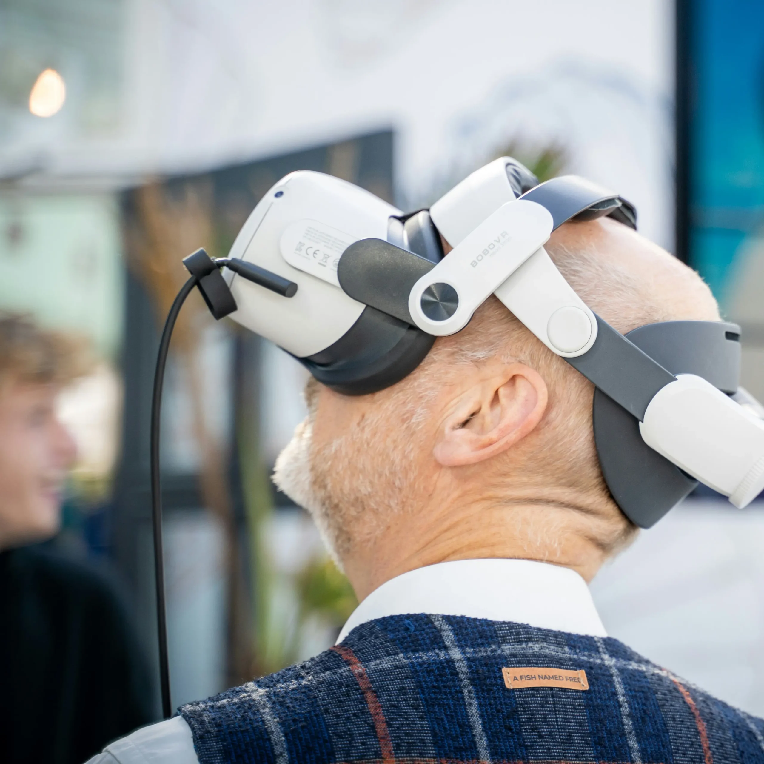 Man met grijze baard en colbert test een VR-headset in een interactieve omgeving.