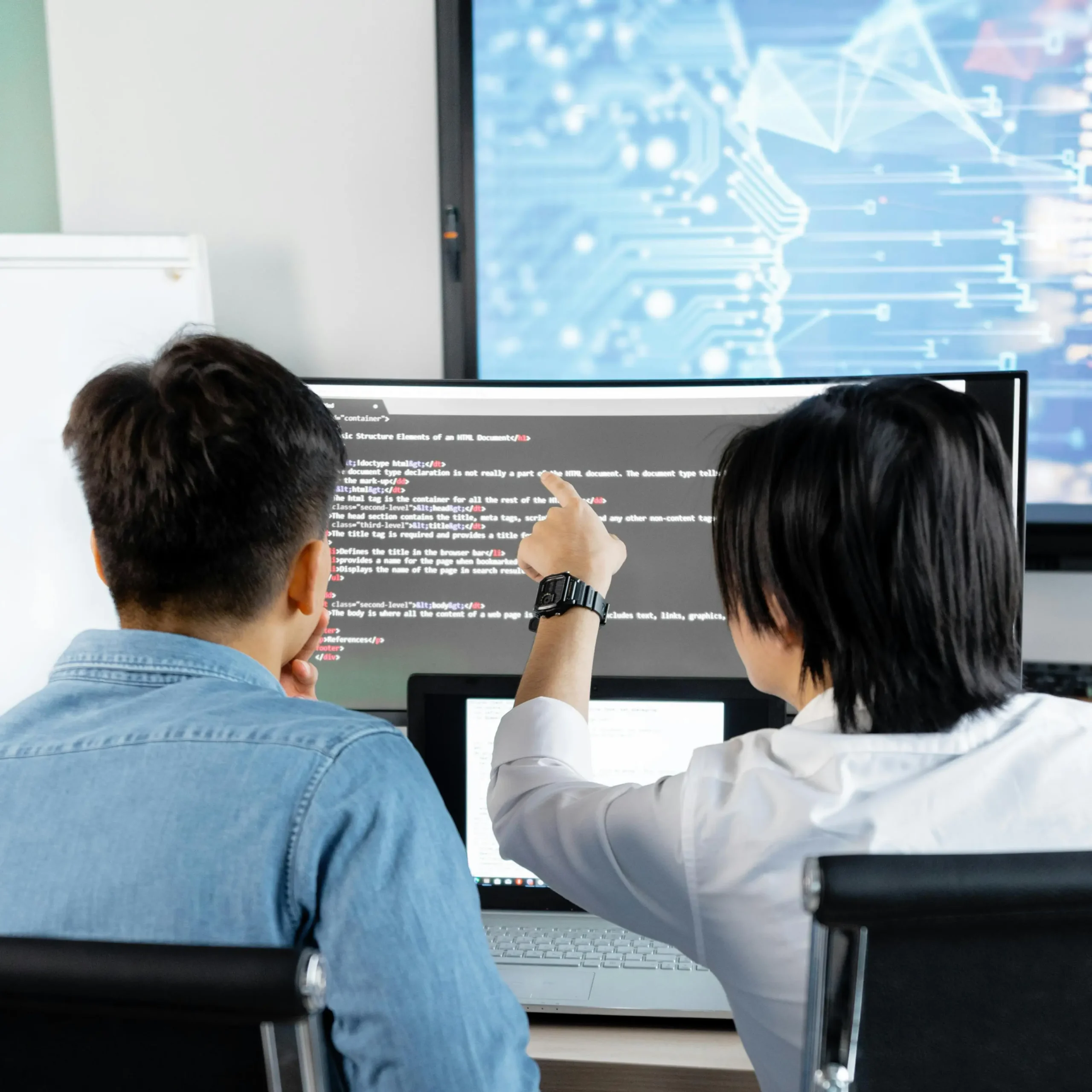 Twee mensen bekijken en bespreken code op een groot computerscherm.
