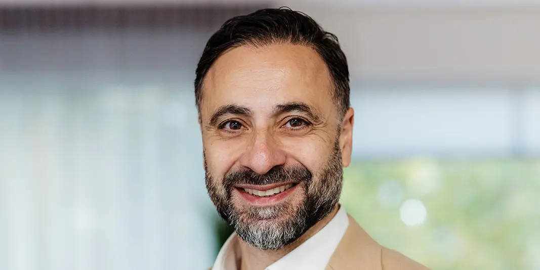 Glimlachende man in een beige colbert voor een zachte, onscherpe achtergrond.