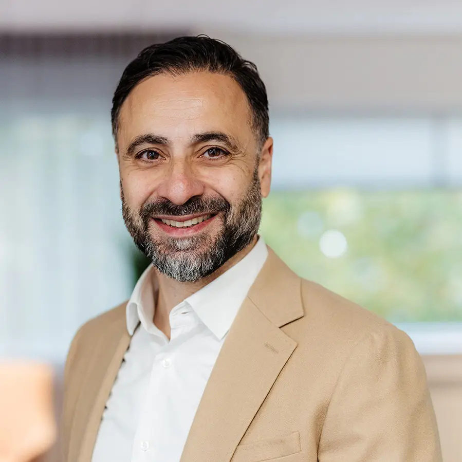 Glimlachende man in een beige colbert voor een zachte, onscherpe achtergrond.