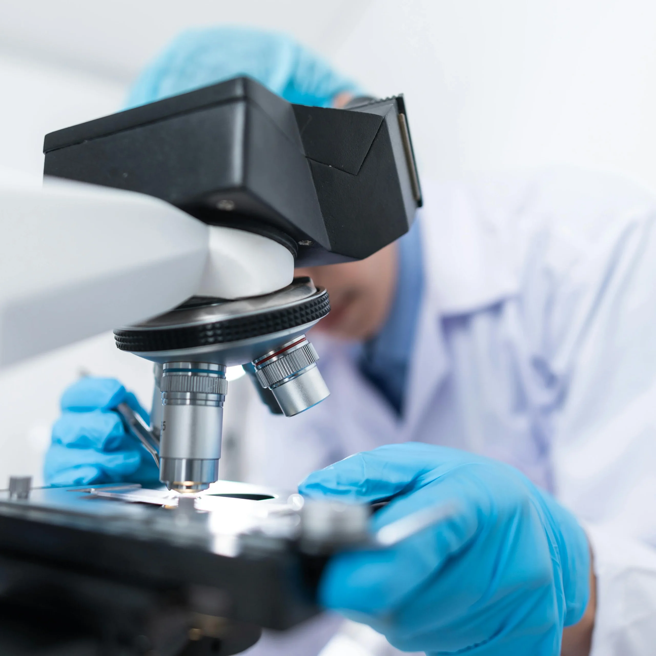 Onderzoeker met handschoenen bekijkt een monster onder een microscoop.