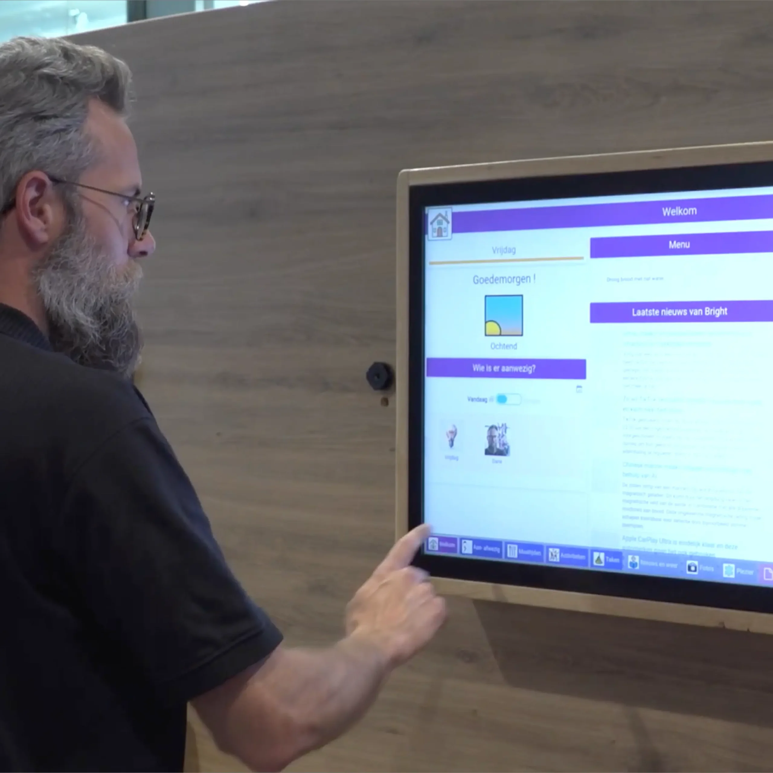 Man met bril en baard bedient een groot aanraakscherm met een digitaal dagprogramma.