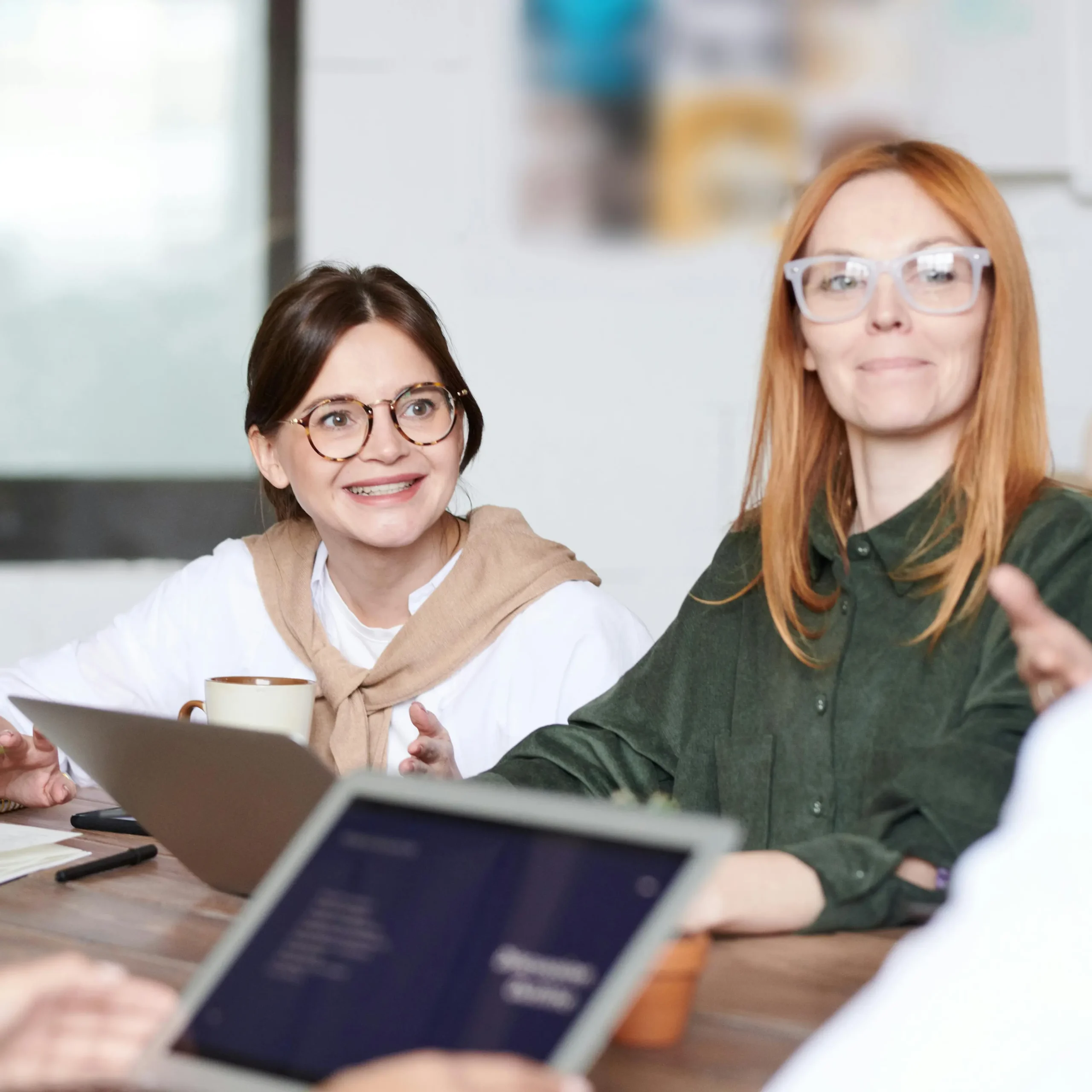 Twee jonge vrouwen zitten in een werkoverleg en glimlachen voor een neutrale achtergrond.
