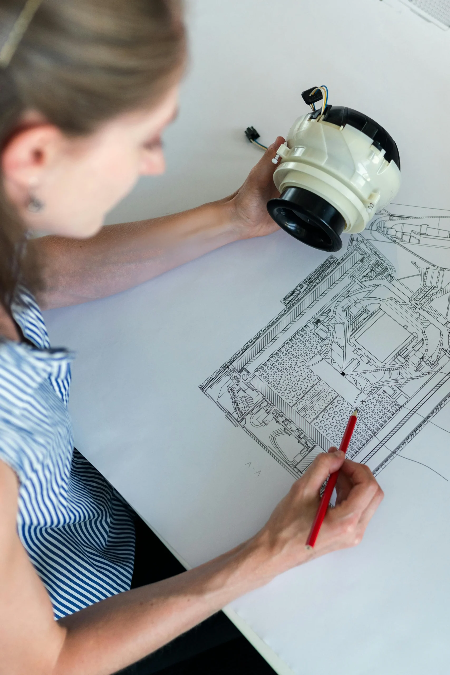 Vrouw bestudeert een technisch onderdeel bovenop een grote technische bouwtekening.