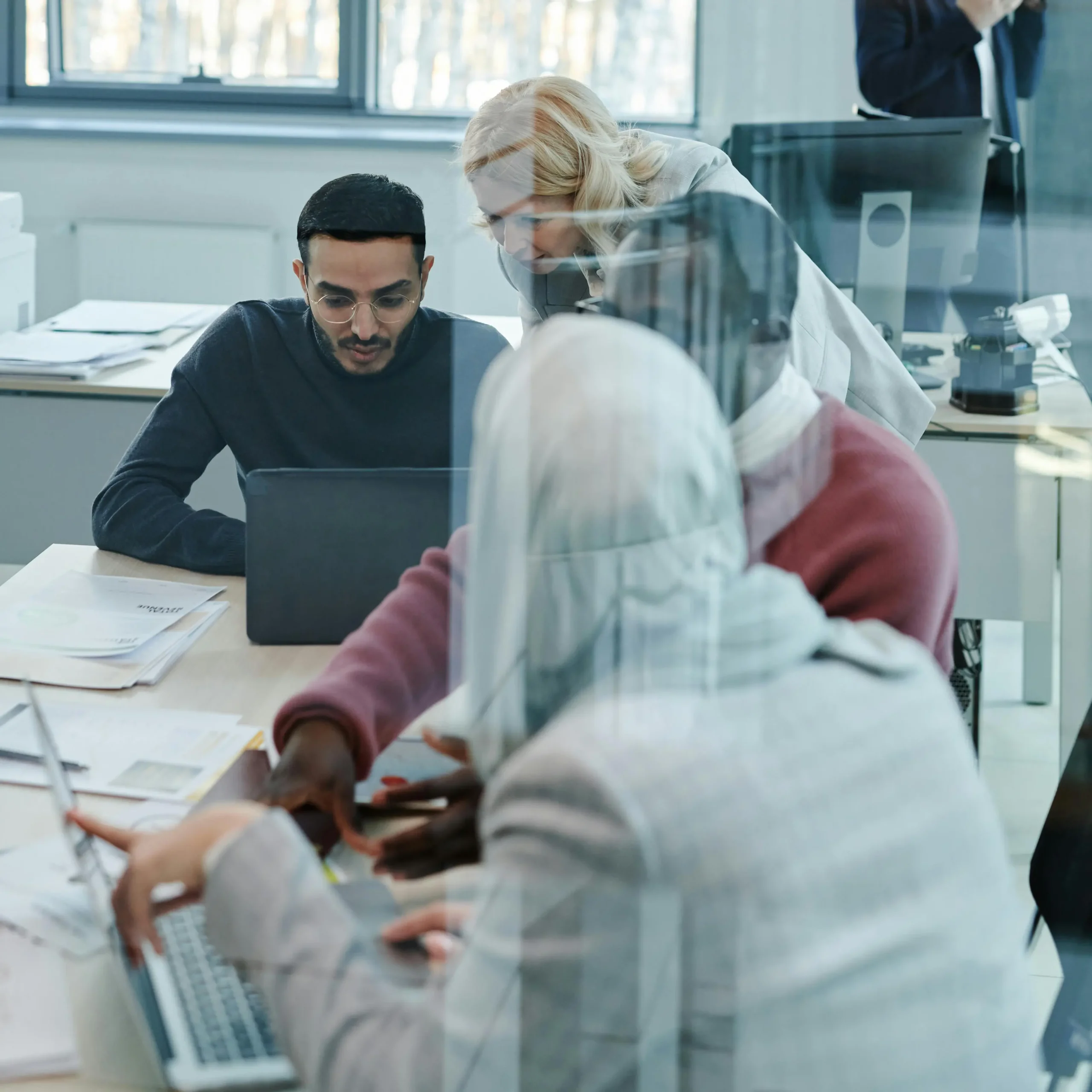 Mensen van diverse achtergronden werken samen rond een tafel met laptops en documenten.