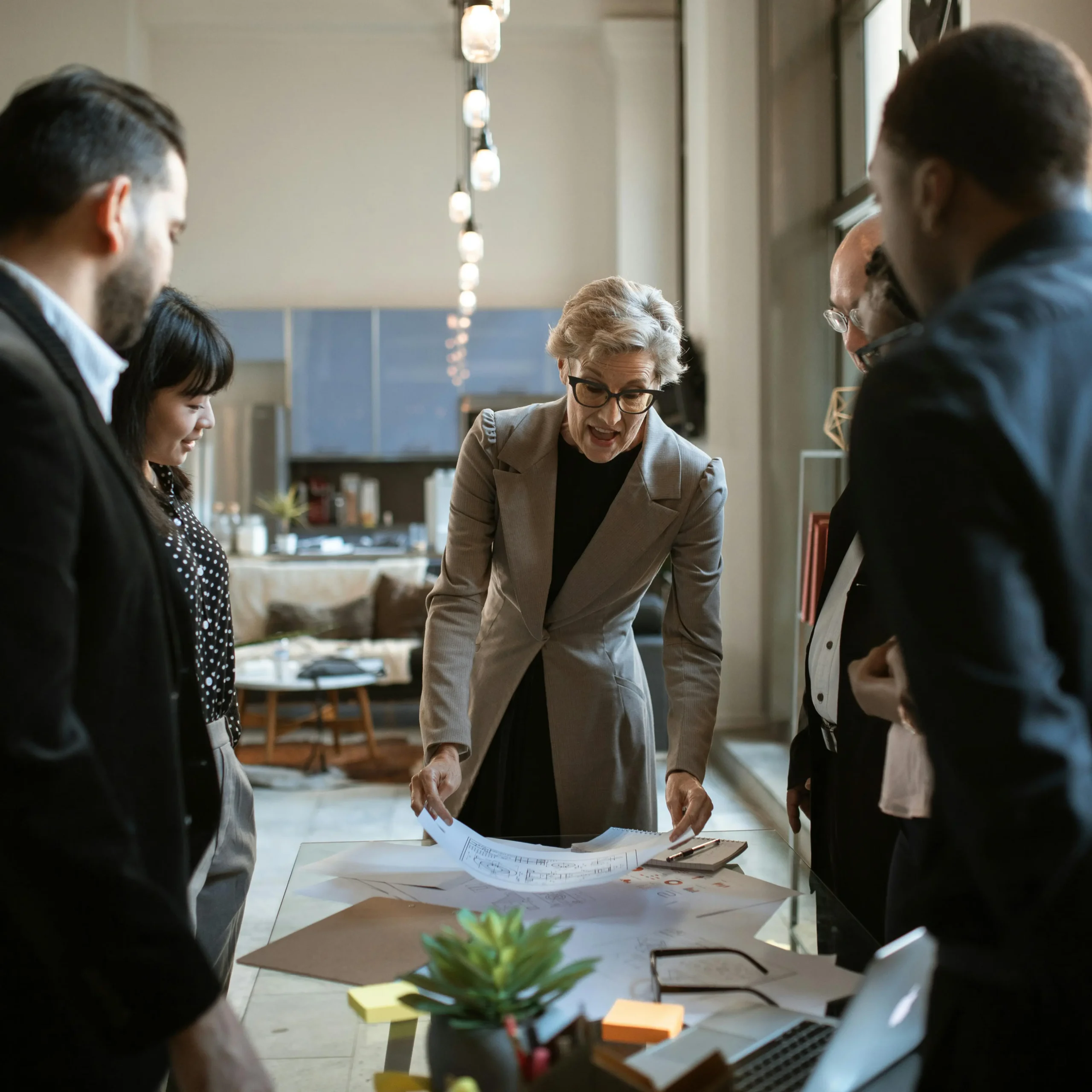 Groep professionals staat rond een tafel terwijl een vrouw haar plannen presenteert.
